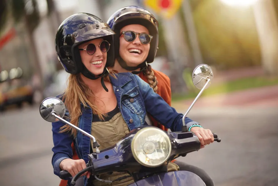 Zwei junge Frauen, die Motorroller fahren