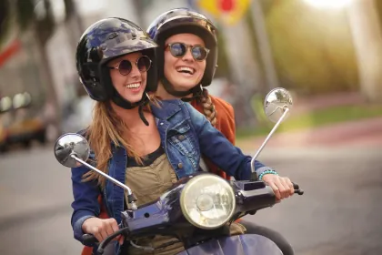 Zwei junge Frauen, die Motorroller fahren